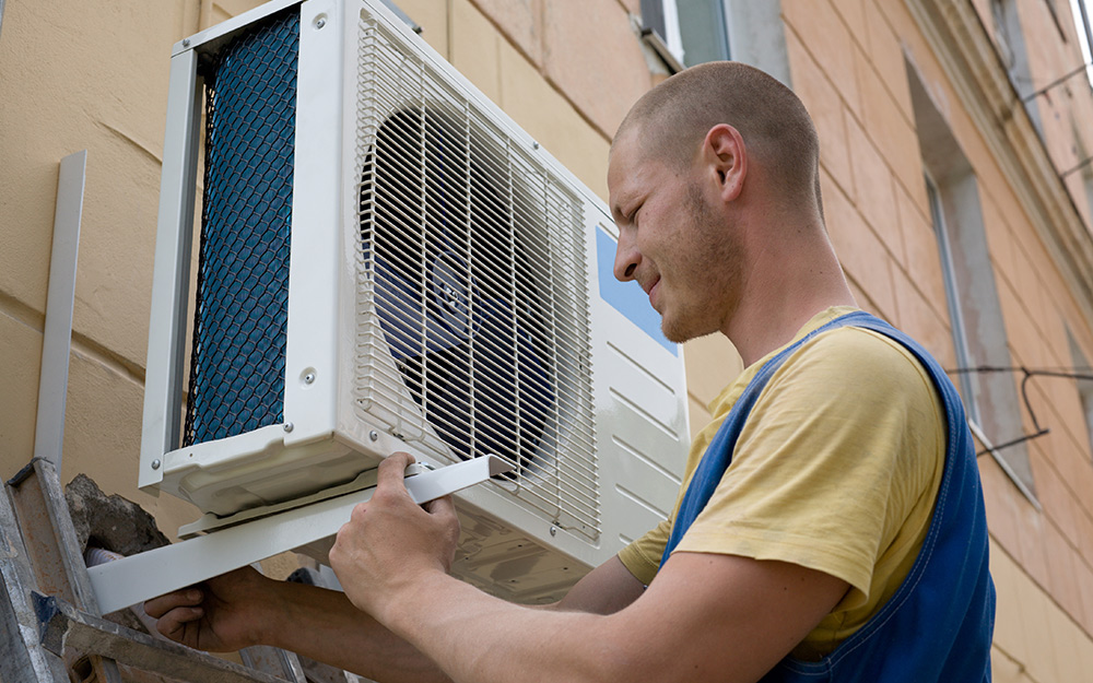 A man installing the outdoor unit of a mini split air conditioner on the exterior of a home