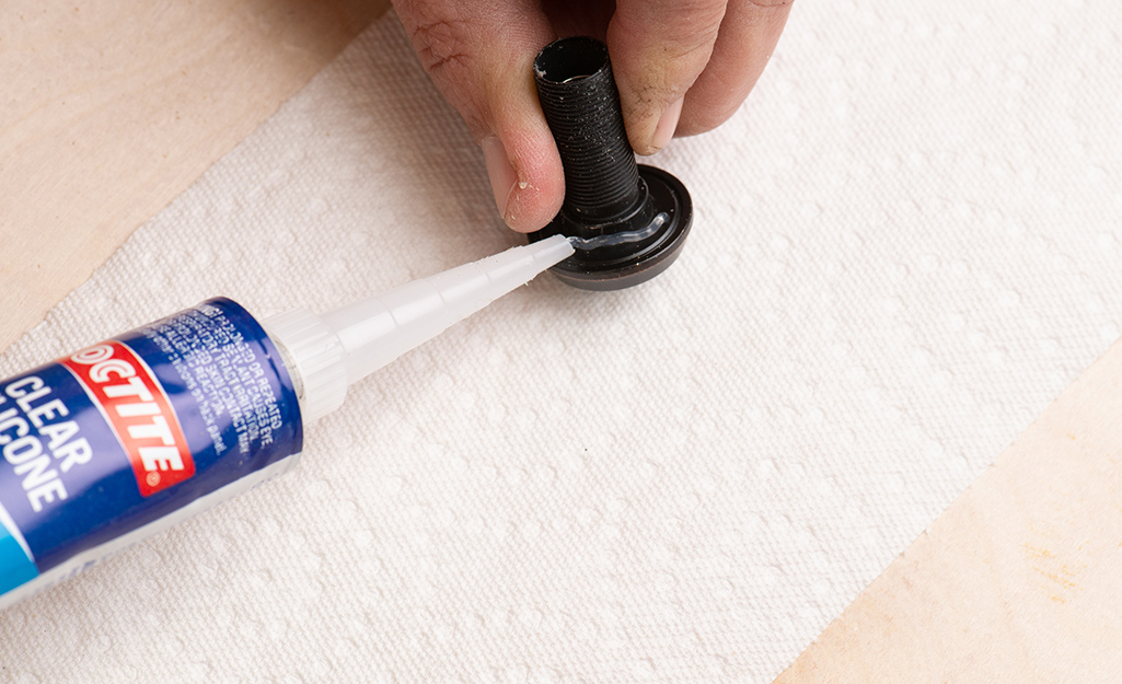 Applying silicone sealant to the lens end of a peephole, or door viewer.