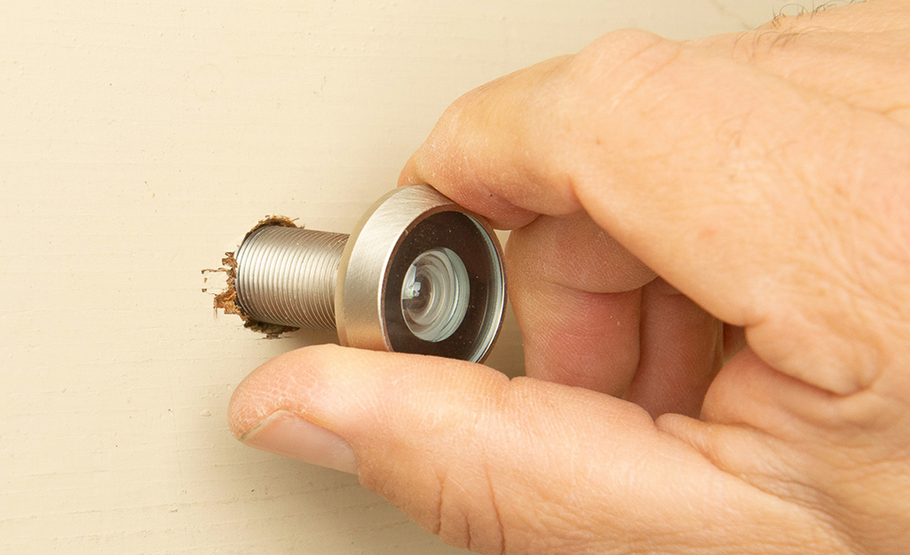A person installs the peephole into the hole drilled in the door.