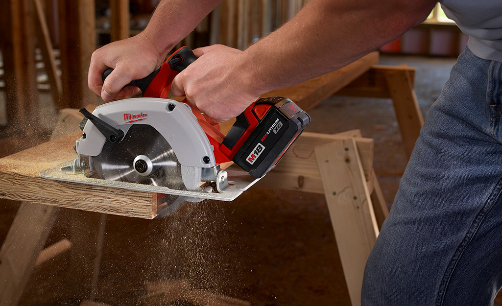 A person uses a circular saw to cut a board.