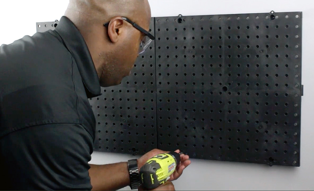 A person uses a power drill to drill holes for hanging a pegboard.