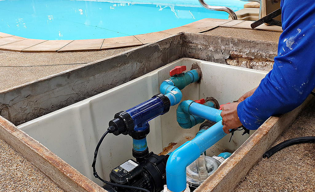 A person opens the cover of a pool pump.