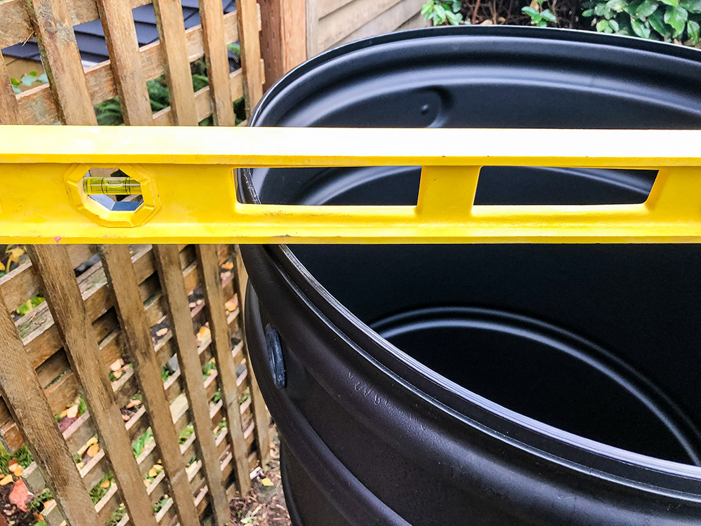 A yellow level sits on top of a black rain barrel.