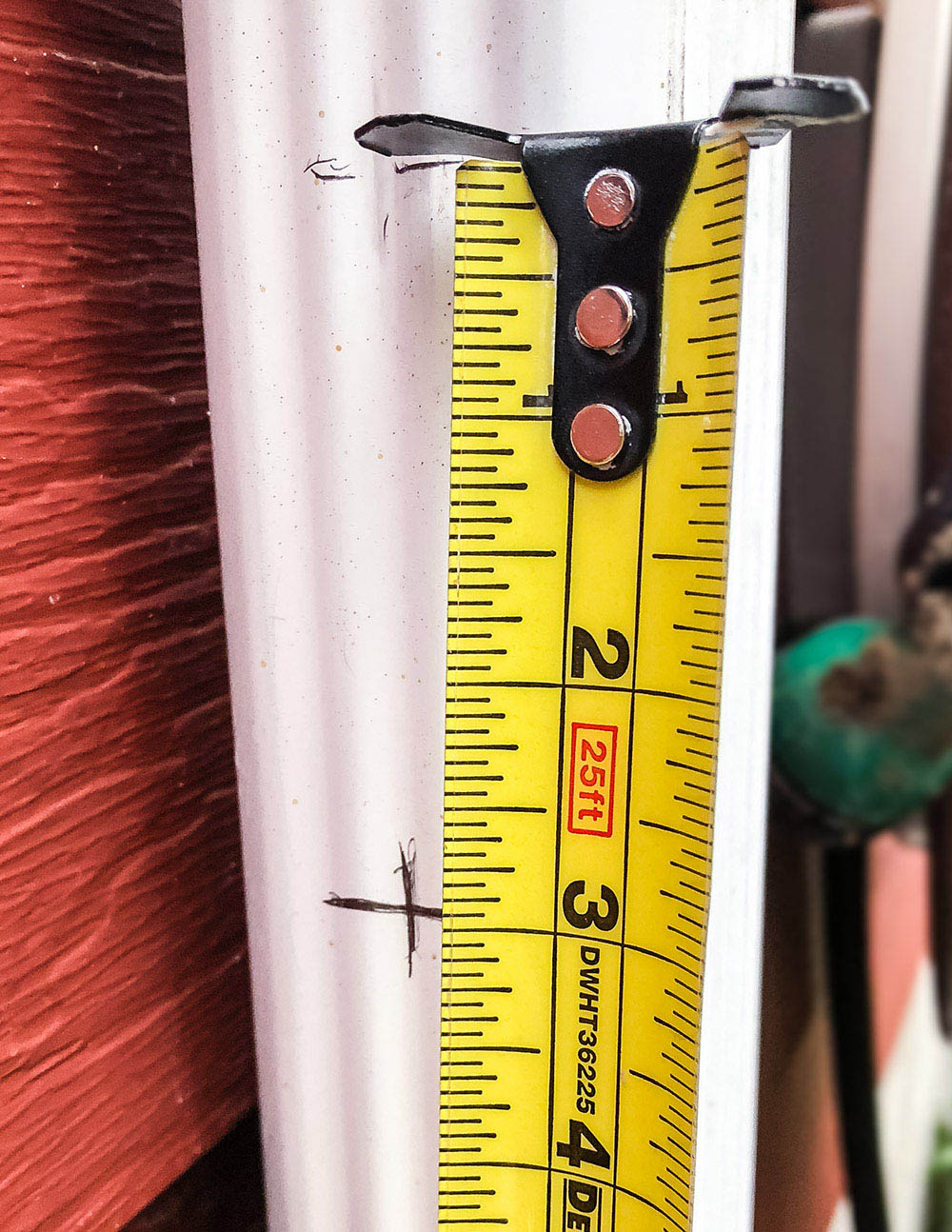 A downspout marked with pencil at 3 inches on a tape measure.