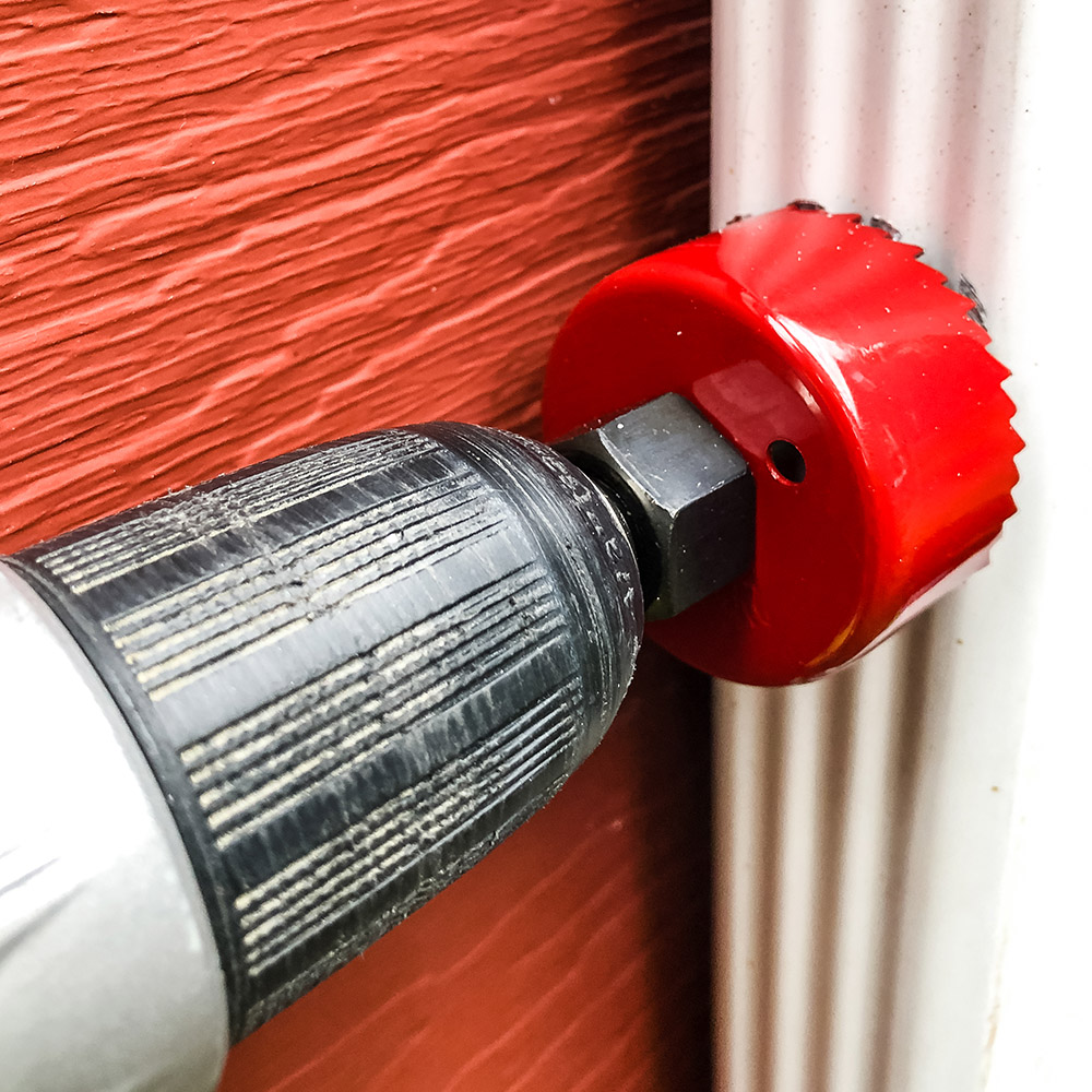 A red hole saw drilling into a downspout.