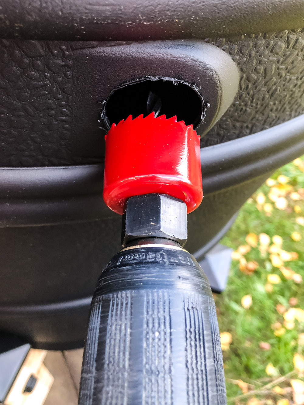 A red hole saw cuts a hole in the side of a rain barrel.