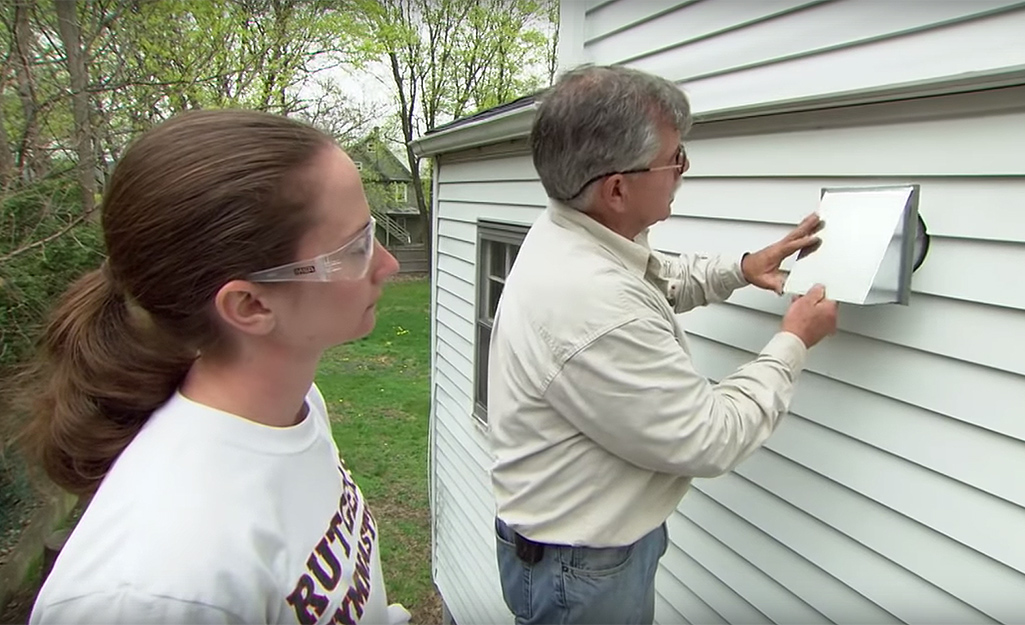 A person installs a duct cap from the outside of a house.