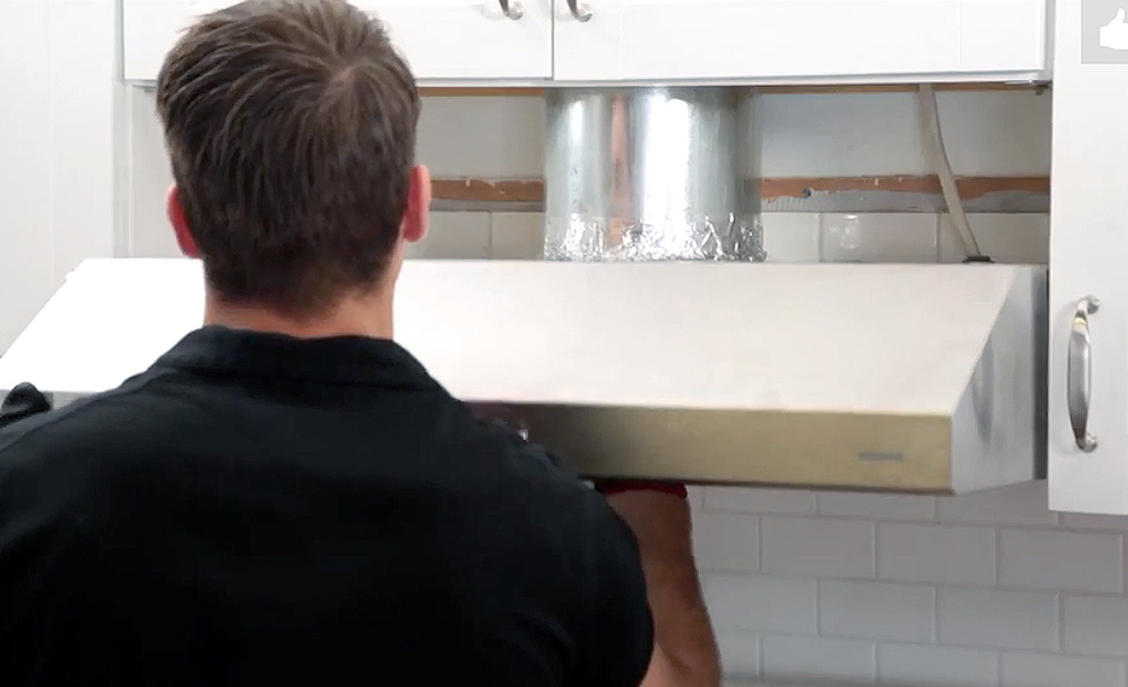 A person installs a new range hood over a stovetop.