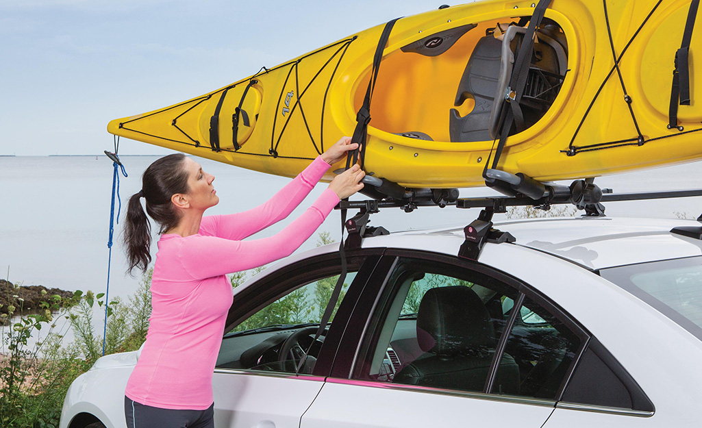 A person secures a yellow kayak to a roof rack.