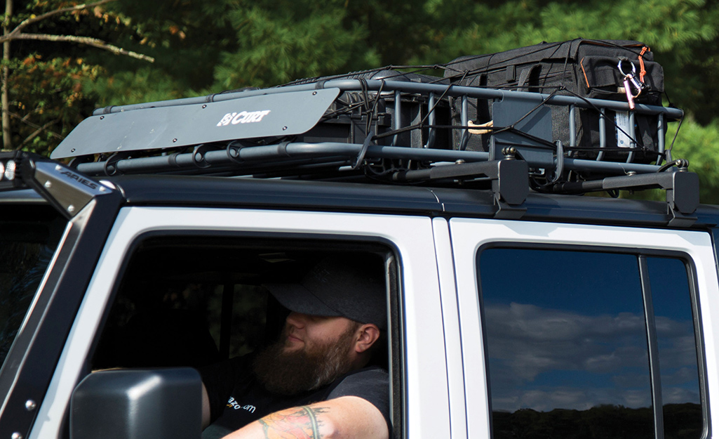 A person in a car with a packed roof rack attached to the roof.
