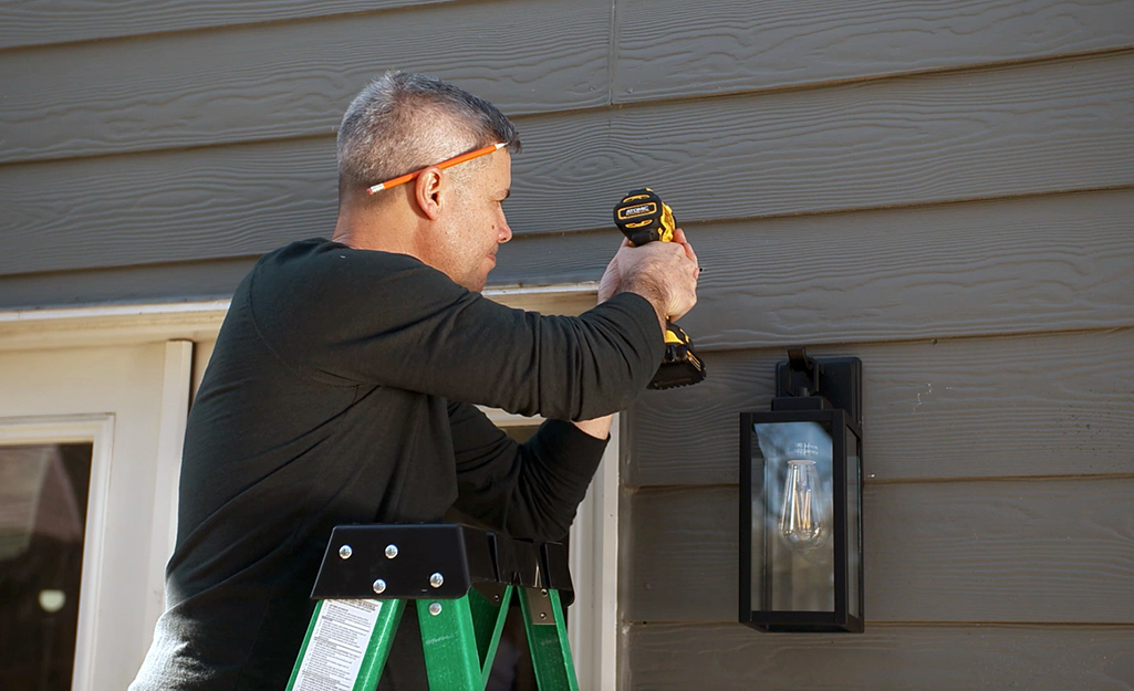 A person drilling into siding to mount a security camera.