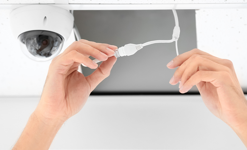 A person attaches the wires of a security camera located on the ceiling. A person attaches the wires of a security camera located on the ceiling.