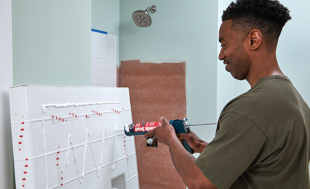 A person applies adhesive to a shower surround panel.