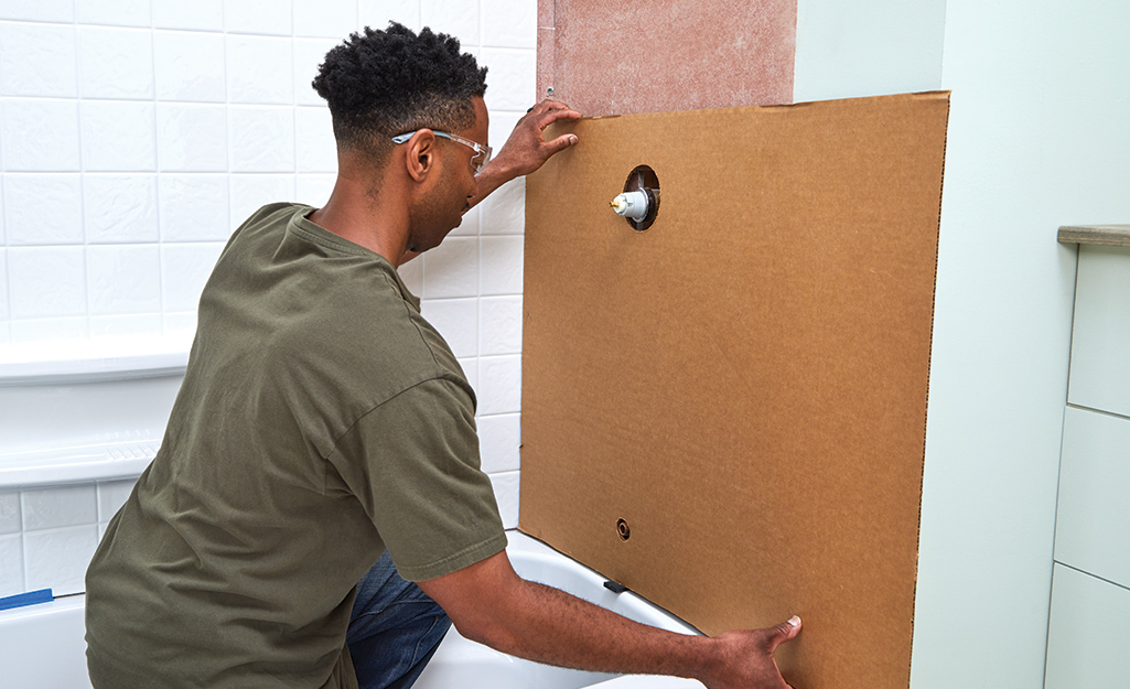 A person places the template of a shower surround on the shower wall.