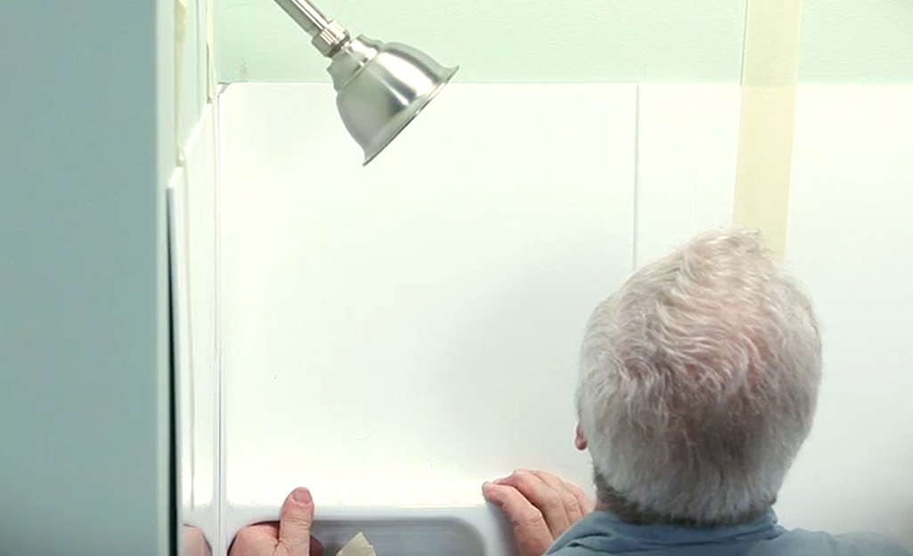 A man fitting a shower surround corner panel in a bath. A man fitting a shower surround corner panel in a bath.