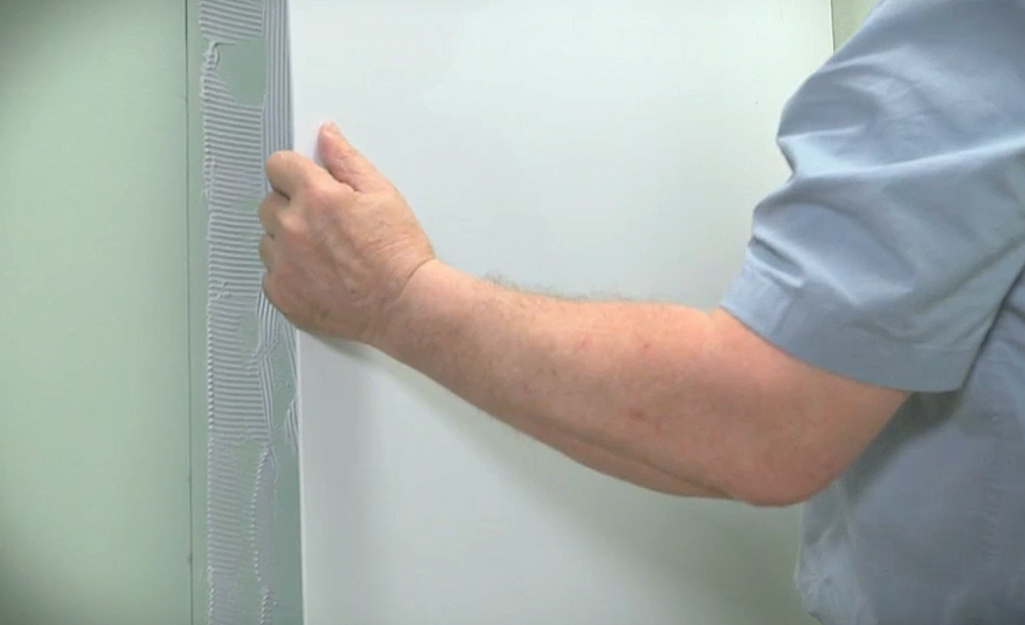 Man pressing a shower surround panel into adhesive spread on a bath wall. Man pressing a shower surround panel into adhesive spread on a bath wall.