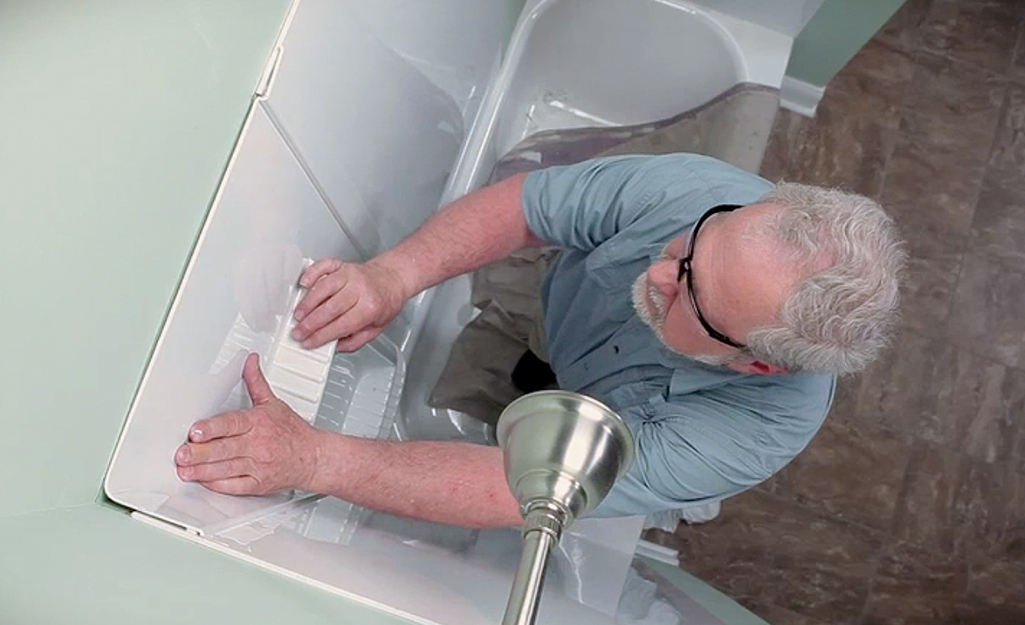 Man installing a corner shower surround panel. Man installing a corner shower surround panel.