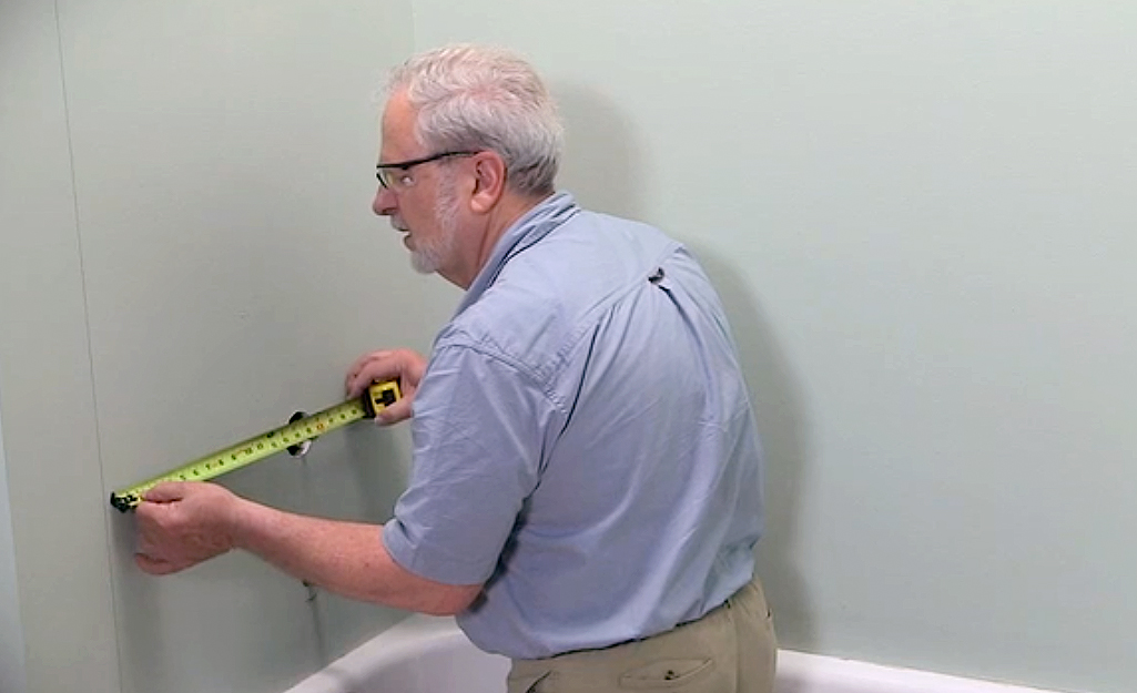 A man measuring the fixture holes in the wall above a tub. A man measuring the fixture holes in the wall above a tub.