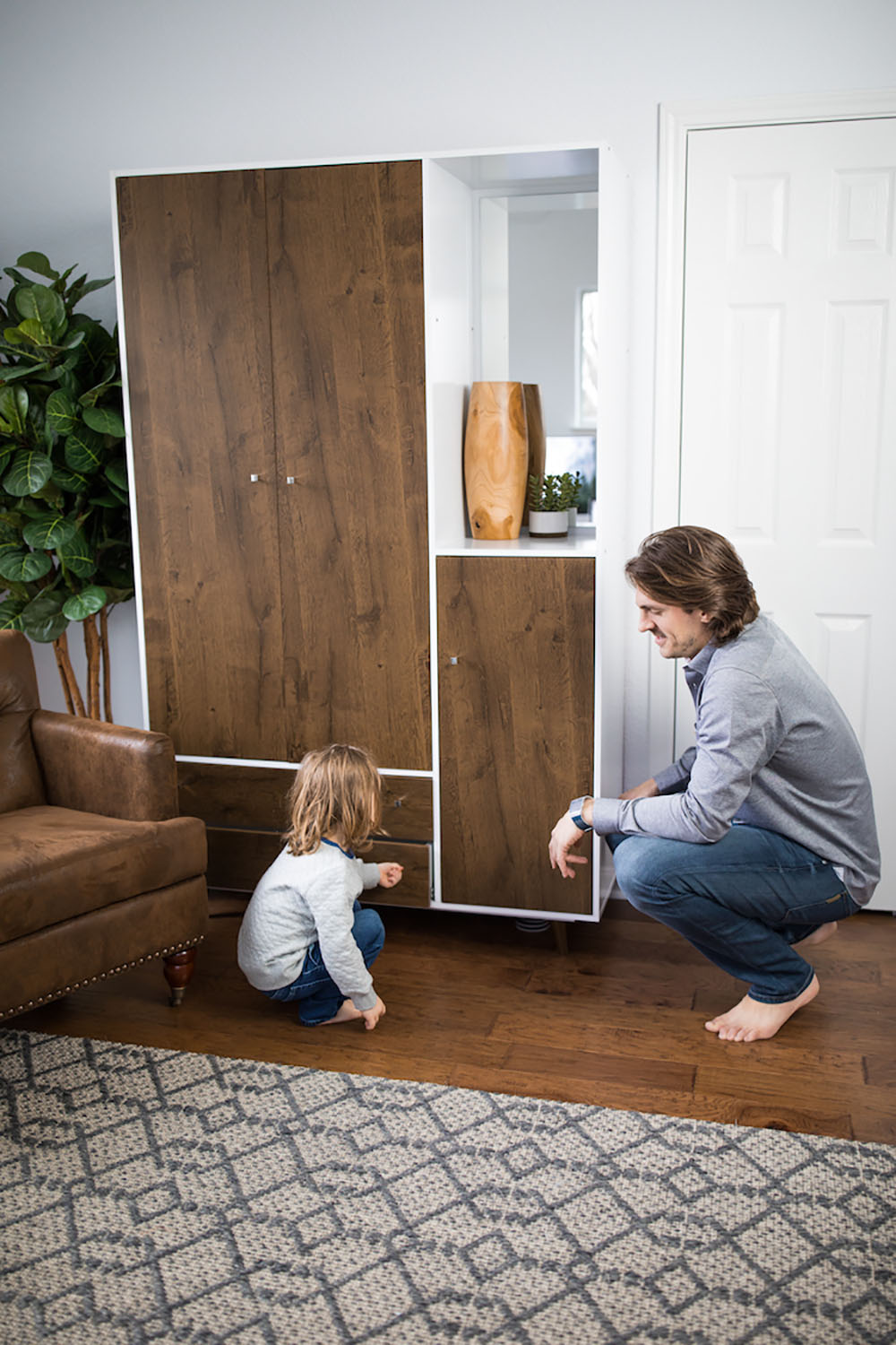 A person and child squatting on the floor looking at a cabinet