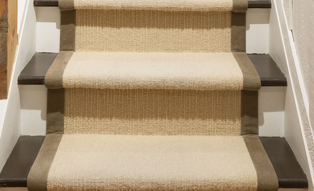 A light brown stair runner with a darker brown edge is centered on a staircase. 