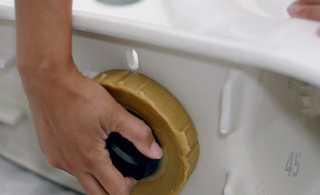 A person inserts a wax ring on the bottom of the toilet.