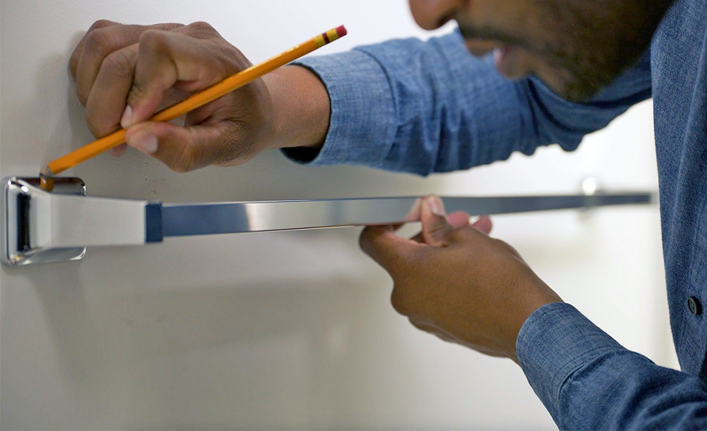 A man marking where a towel bar will be placed in a bath.