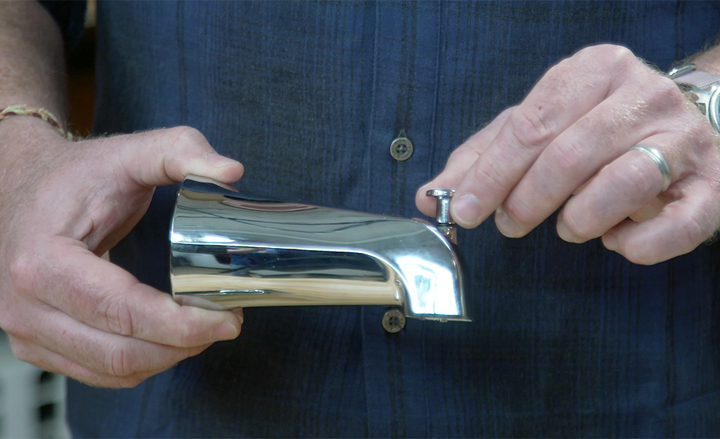 A man holds a tub spout with a diverter valve. 