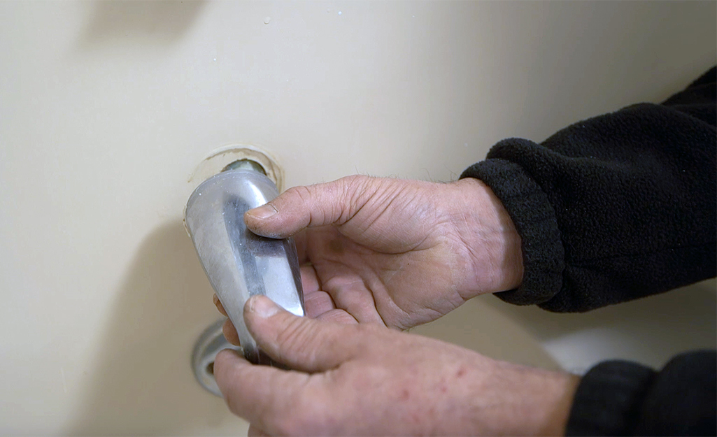 A person removes an old tub spout. 