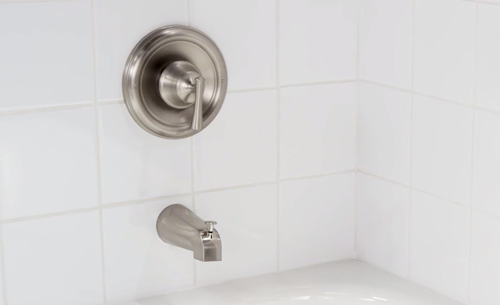 A new tub faucet and shower hardware installed in a white tile bath. A new tub faucet and shower hardware installed in a white tile bath.