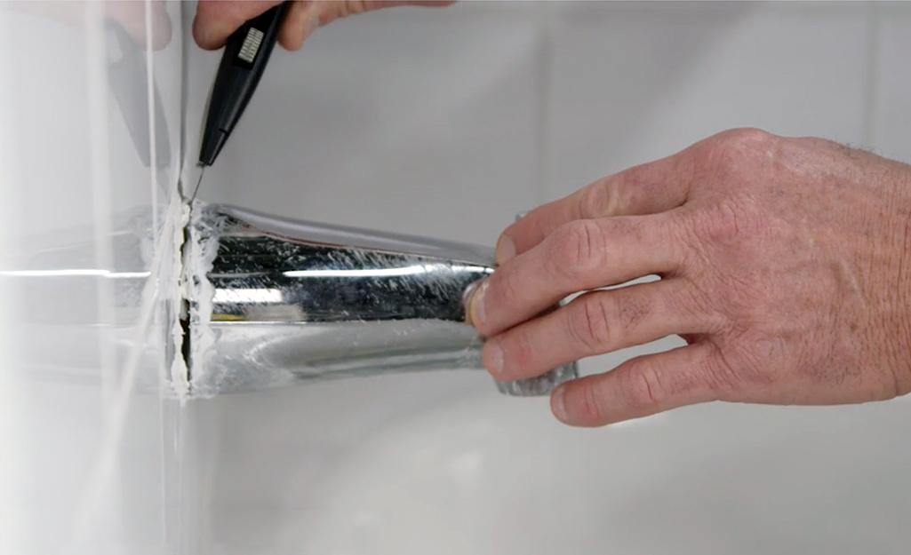 Man loosening an old tub spout with utility knife. Man loosening an old tub spout with utility knife.