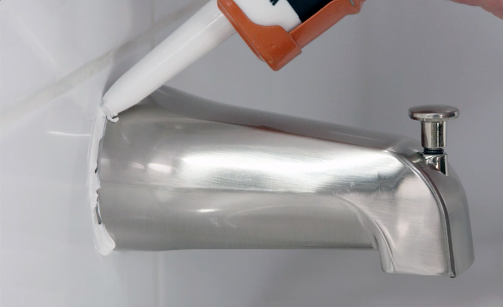 Someone caulking around a new tub spout. Someone caulking around a new tub spout.