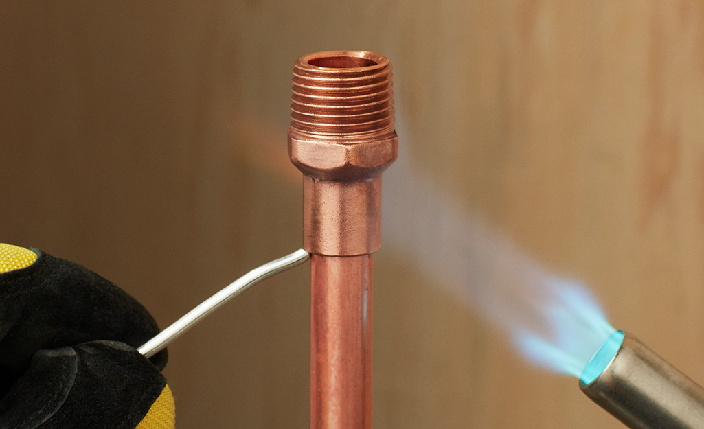 A person soldering a connection on a copper pipe.