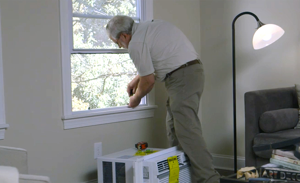 A person securing a support bracket to install a window air conditioner.