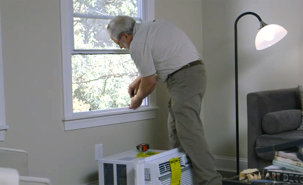 Une personne fixant un support pour installer un climatiseur de fenêtre.