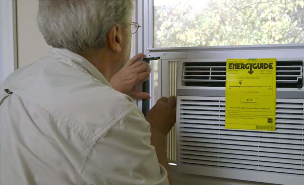 Une personne qui prolonge le panneau latéral d'un climatiseur lors de l'installation d'un climatiseur de fenêtre.