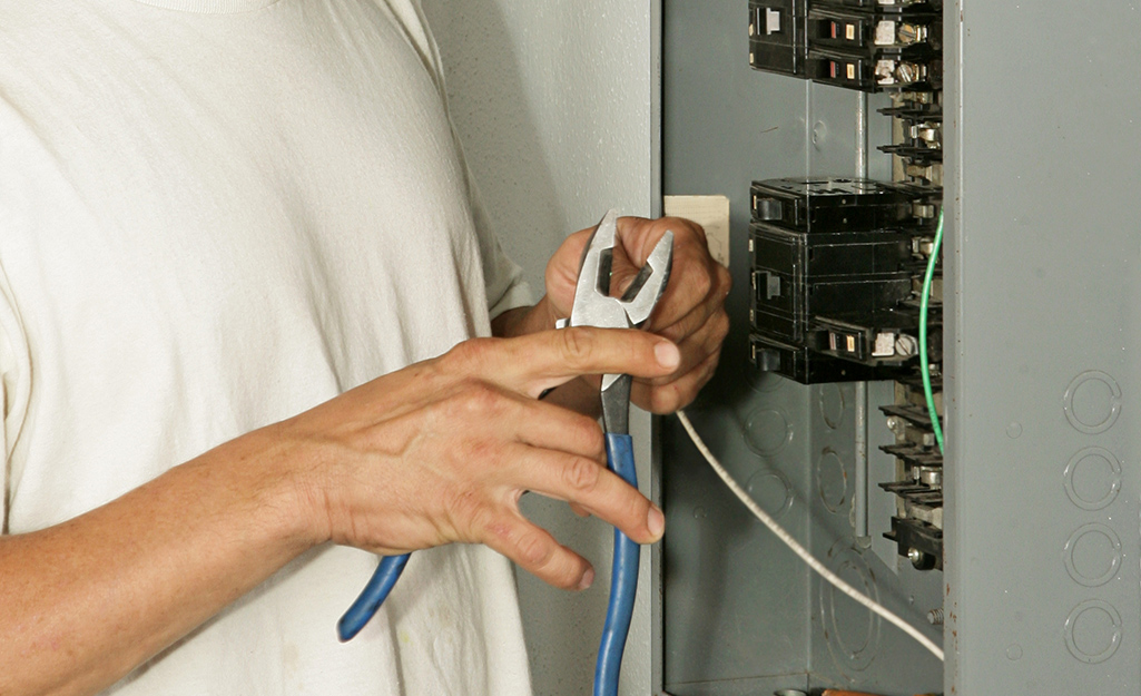 A man using wire cutters on a white wire in a circuit breaker.