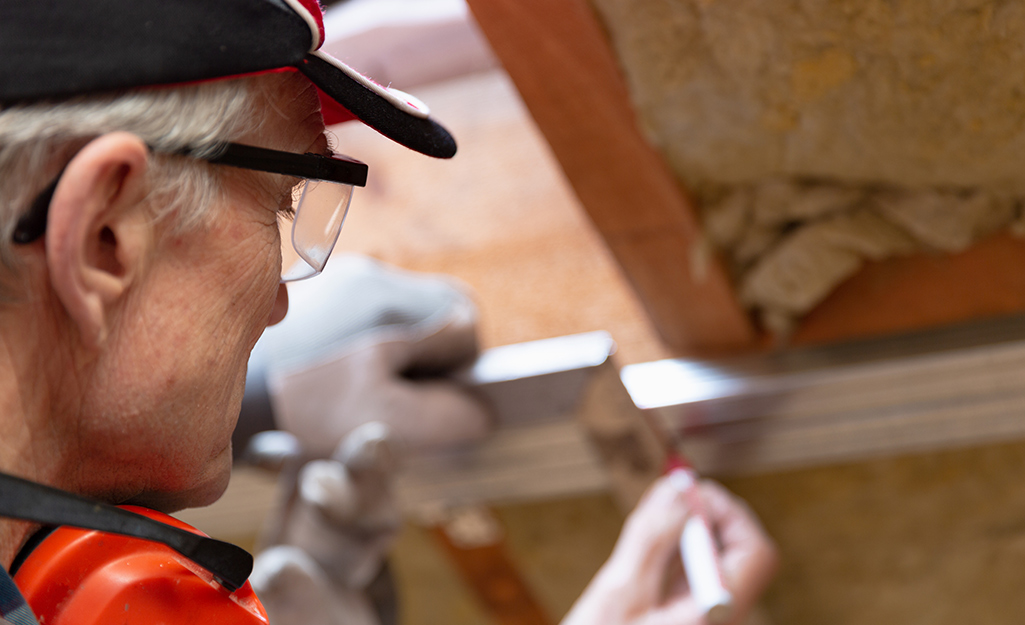 A person marks pilot holes in an attic ladder frame before drilling.
