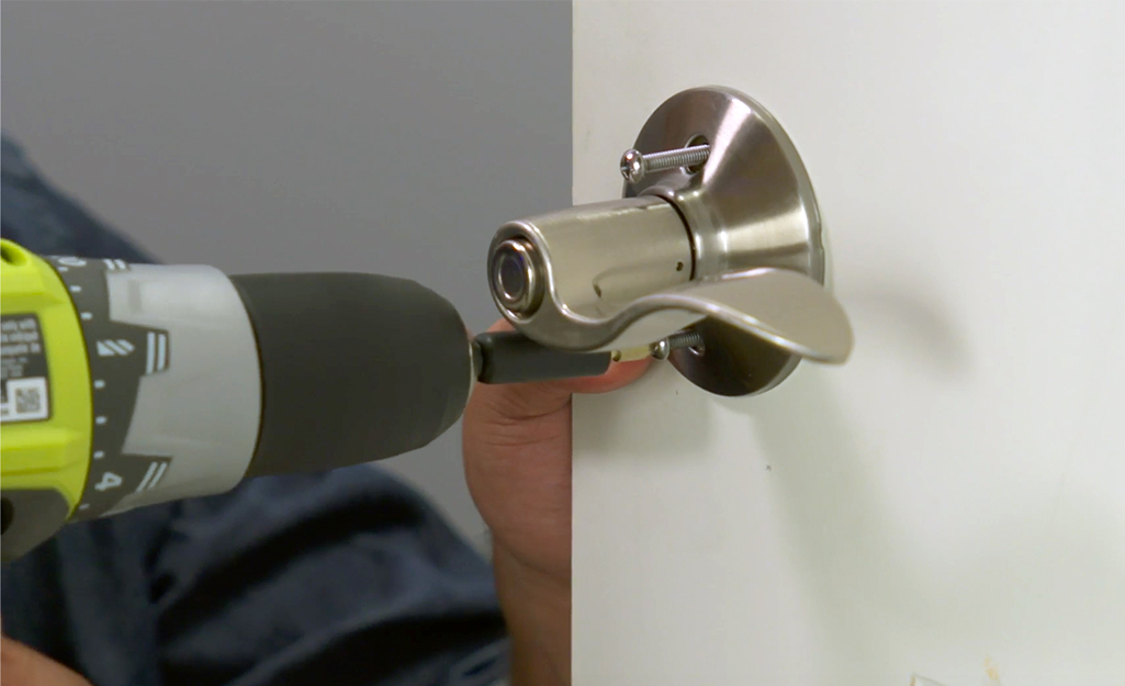 A person using a drill to attach a door handle to a door.