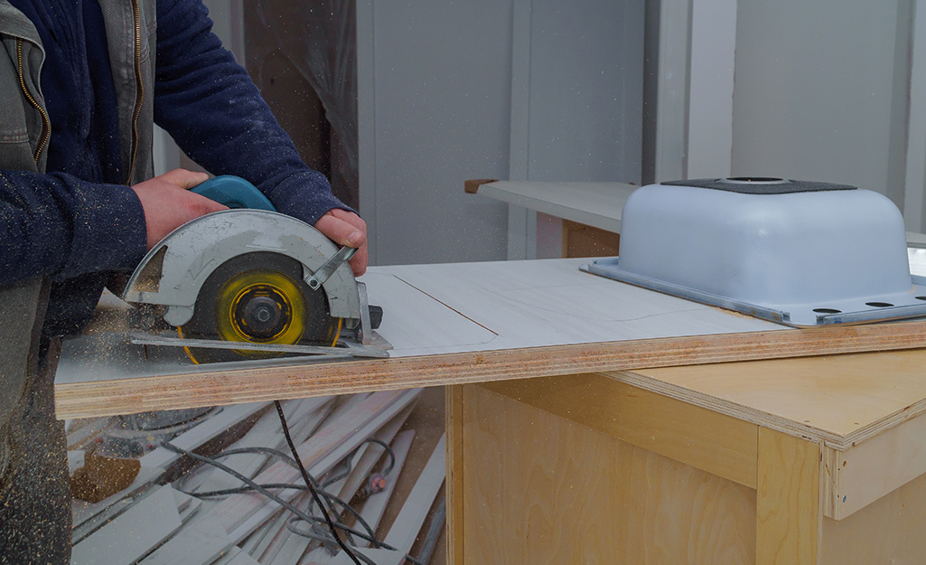 A person uses a circular saw to cut a sink hole in a countertop. A person uses a circular saw to cut a sink hole in a countertop.