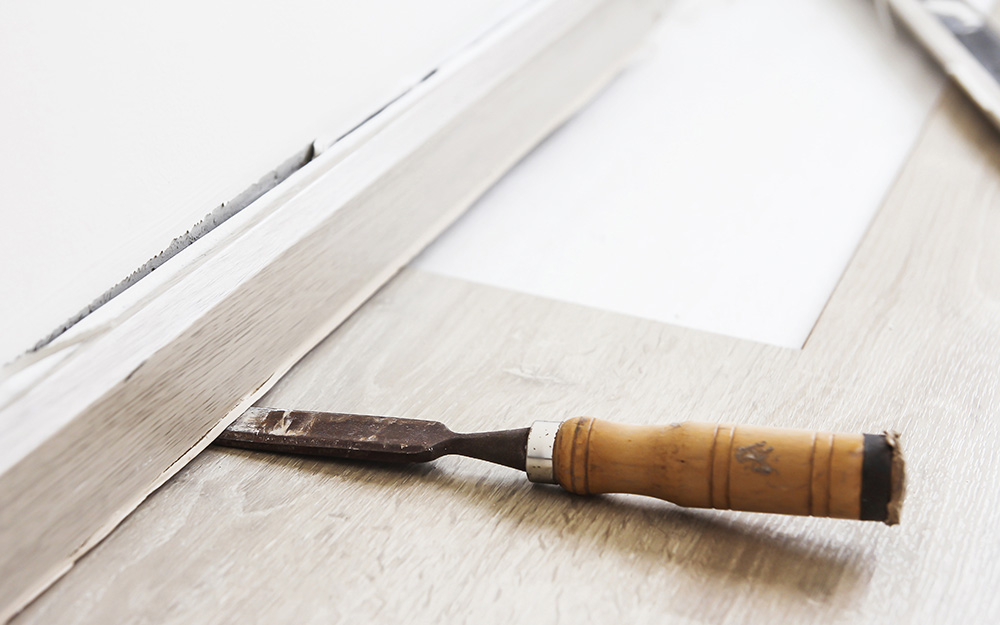 A chisel is used to pry off old baseboard to get the wall ready for beadboard wainscoting installation.