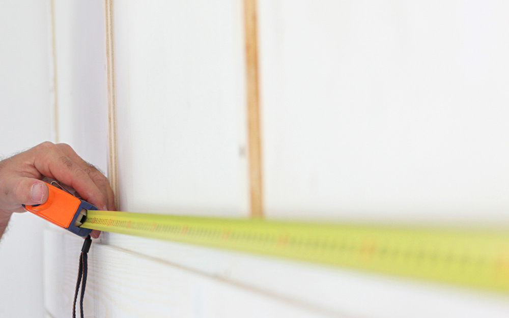 A person uses a tape measure to measure sections on a wall.