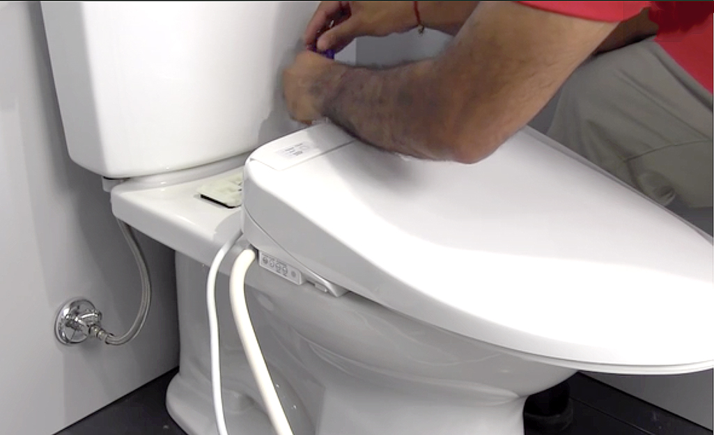 A person hooks up the water supply hose to the back of a bidet toilet seat.
