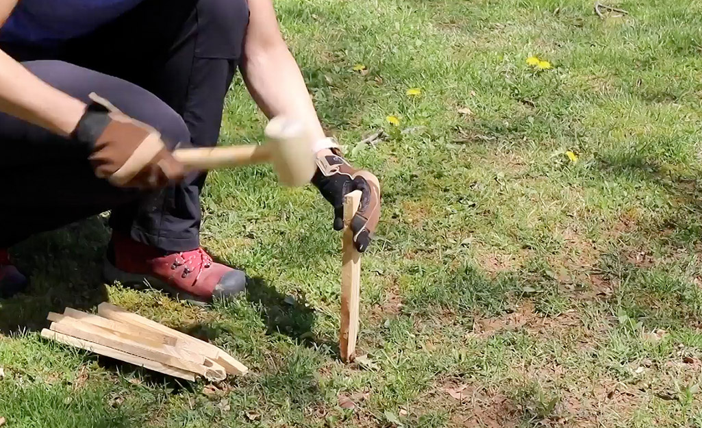 A person uses a mallet to hammer a stake into the lawn.