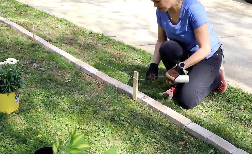 A person attaches a length of Mason's line to a stake marking brick edging. 