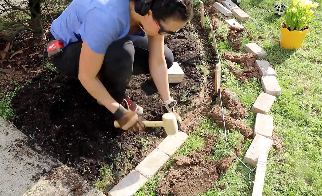 A person uses a mallet to tap bricks into the soil.