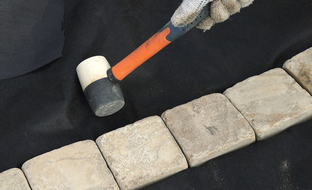 Someone using a mallet to align concrete bricks to edge a bed. Someone using a mallet to align concrete bricks to edge a bed.