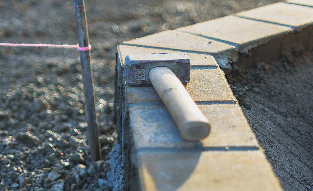 A sledgehammer sitting on top of a row of brick edging around a garden bed. A sledgehammer sitting on top of a row of brick edging around a garden bed.