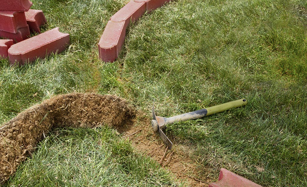 Someone using a mattock to make a curve in the lawn to install brick edging. Someone using a mattock to make a curve in the lawn to install brick edging.