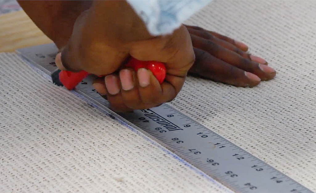 A person uses a metal ruler as a straightedge as they cut the backside of carpet before it is installed.