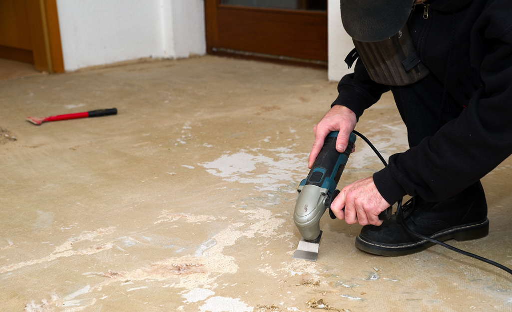 A man wearing a safety mask uses a sander to prepare a subfloor.